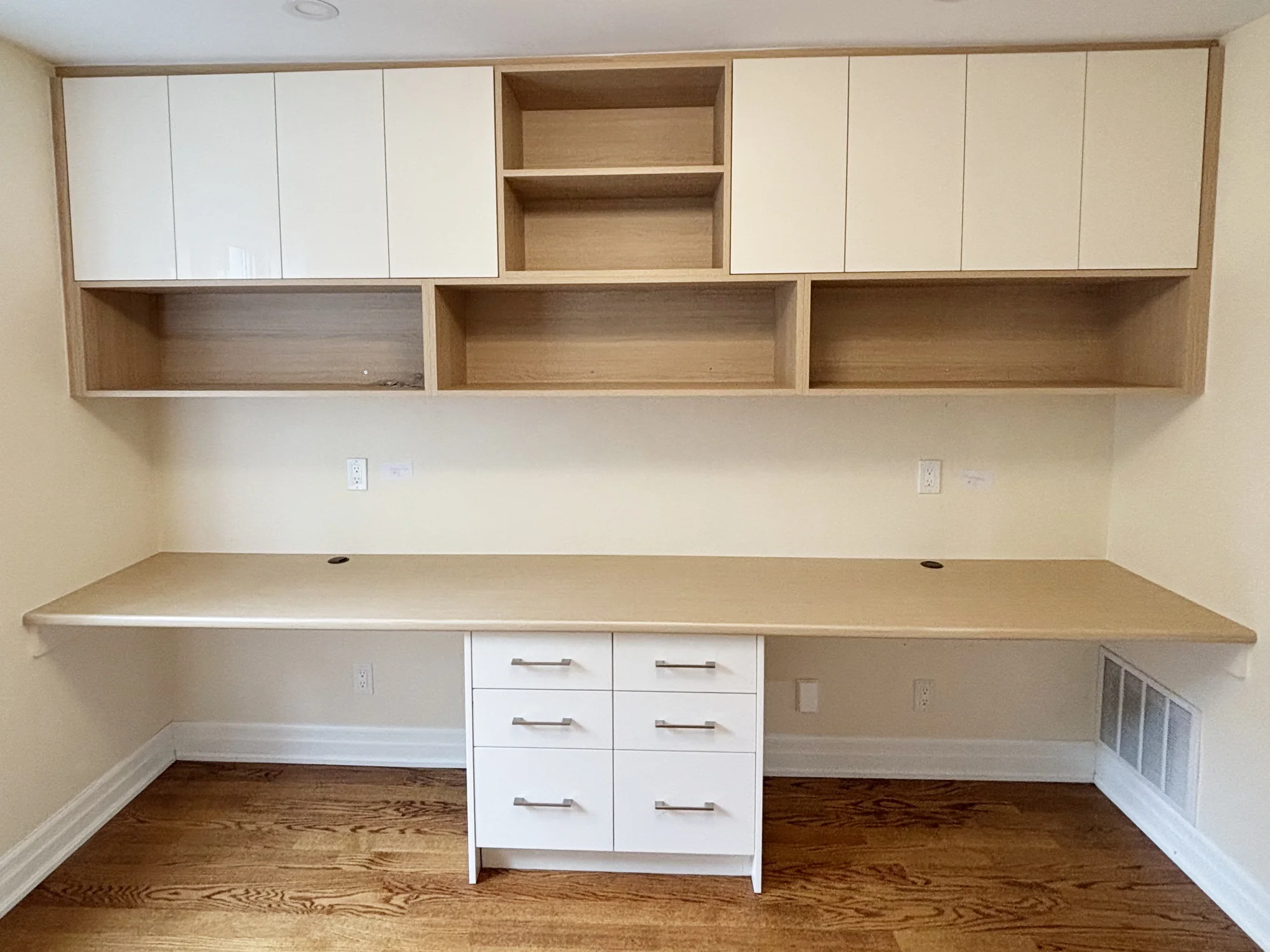 Completed home office with a long fitted desk, cabinets, and open shelving.