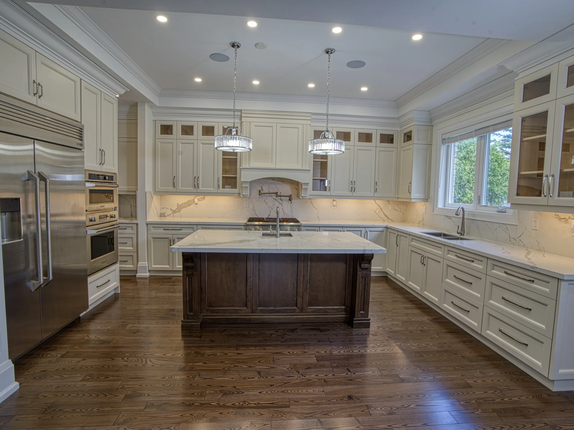 Completed Traditional kitchen with detailed white cabinetry, layered crown moulding, glass display doors, and a dark wood island.