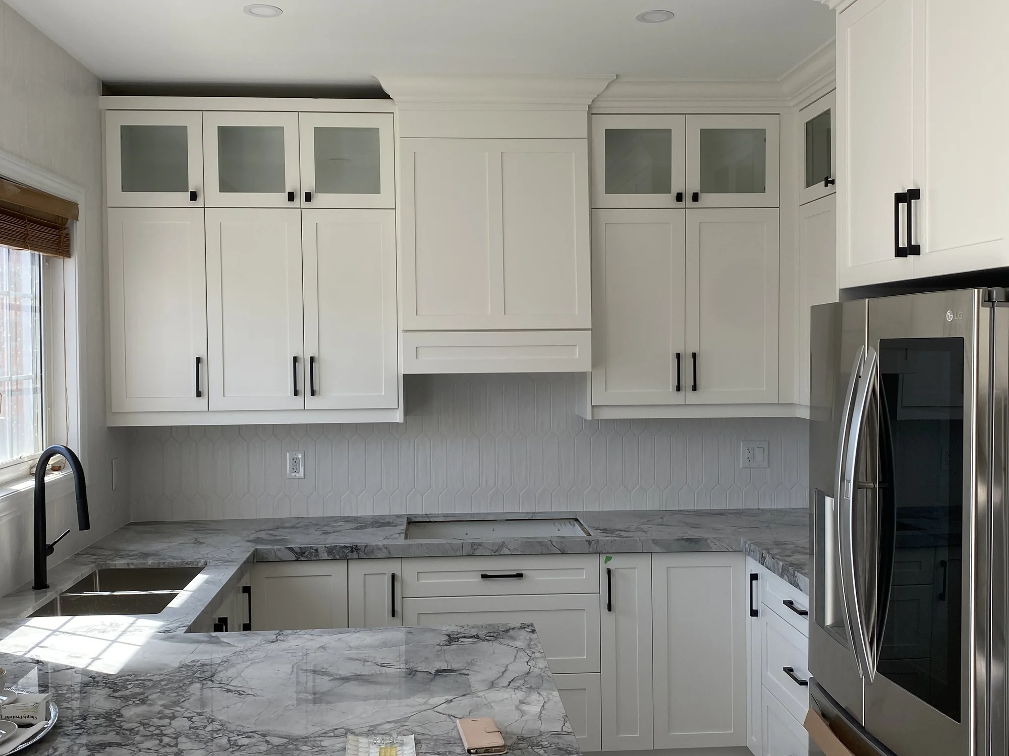Transitional white kitchen cabinetry with Shaker doors, simple dark pulls, restrained crown detail, glass cabinets, and clean proportions.