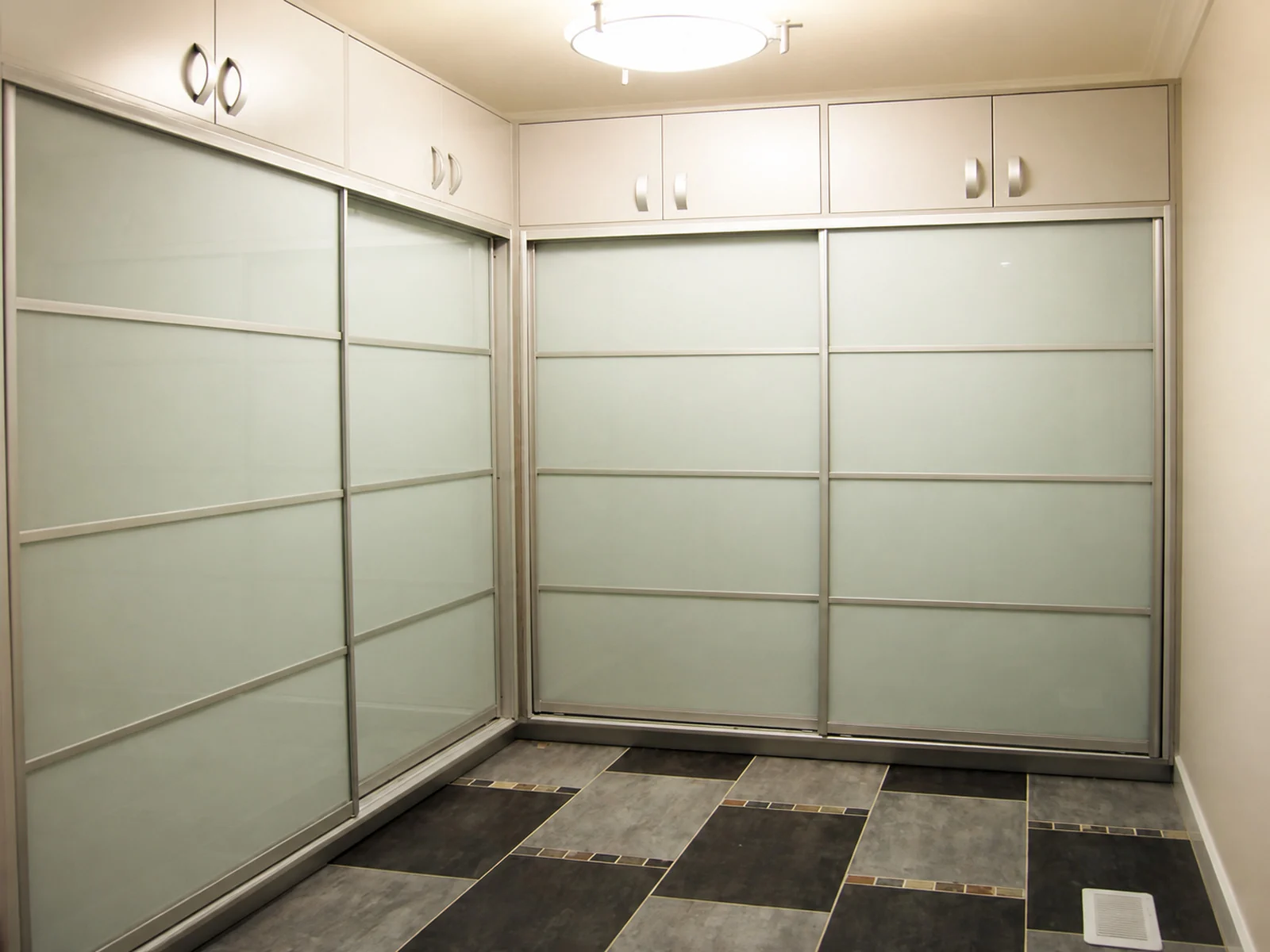 Walk-in closet with sliding glass doors below hinged overhead cabinets.