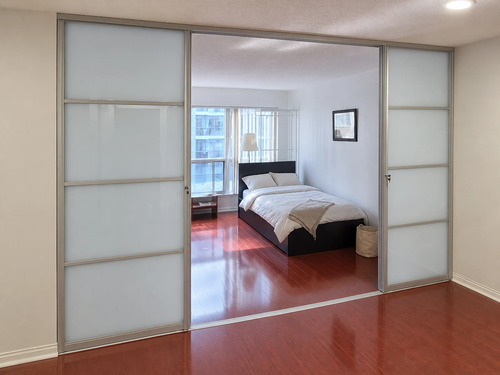 Silver-framed frosted sliding doors converting a condo den into a private bedroom.