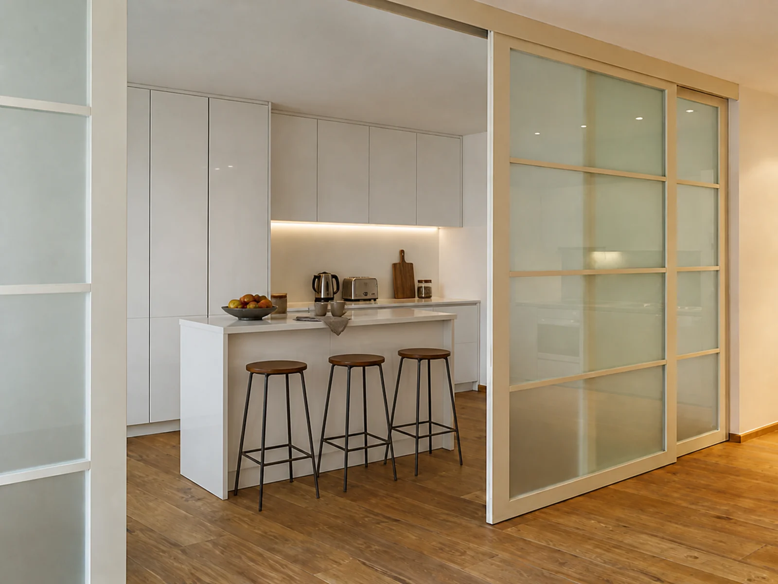 MDF-framed glass sliding divider separating a bright kitchen from the adjoining interior.